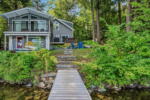 A two-story house with a dock leading to a small stream.