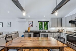 A modern kitchen with a wooden dining table, grey cabinets, and a large window. - Lakefront Cottage w/ Hot Tub & Dock on Lake Rescue (Ludlow)