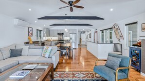 A spacious living room with a high ceiling, a ceiling fan, and a kitchen in the background. - Lakefront Cottage w/ Hot Tub & Dock on Lake Rescue (Ludlow)