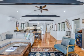 A spacious living room with a high ceiling, a ceiling fan, and a kitchen in the background. - Lakefront Cottage w/ Hot Tub & Dock on Lake Rescue (Ludlow)