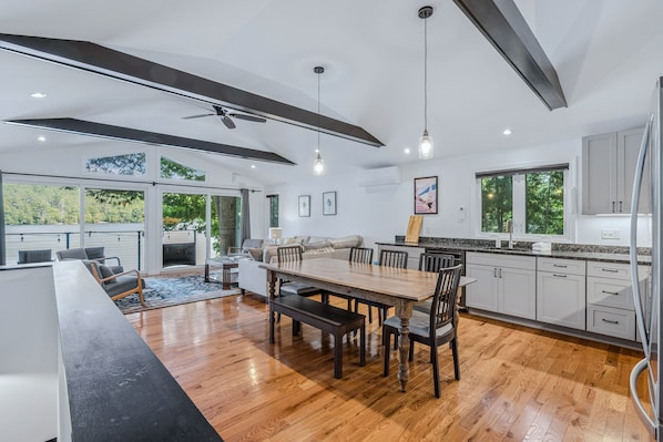 A modern kitchen with a dining area, wooden flooring, and large windows.