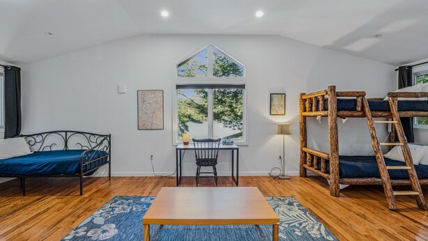 A room with a bunk bed, a desk, a chair, a table, a window with a view, and a lamp. - Lakefront Cottage w/ Hot Tub & Dock on Lake Rescue (Ludlow)