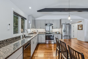 A modern kitchen with granite countertops, stainless steel appliances, and a wooden dining table.