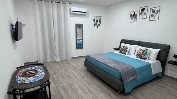 A bedroom with a bed, a desk, and a chair. There is an air conditioning unit on the wall, a window with curtains, and a wall-mounted TV. - Cristofaro home 2 (Palermo)