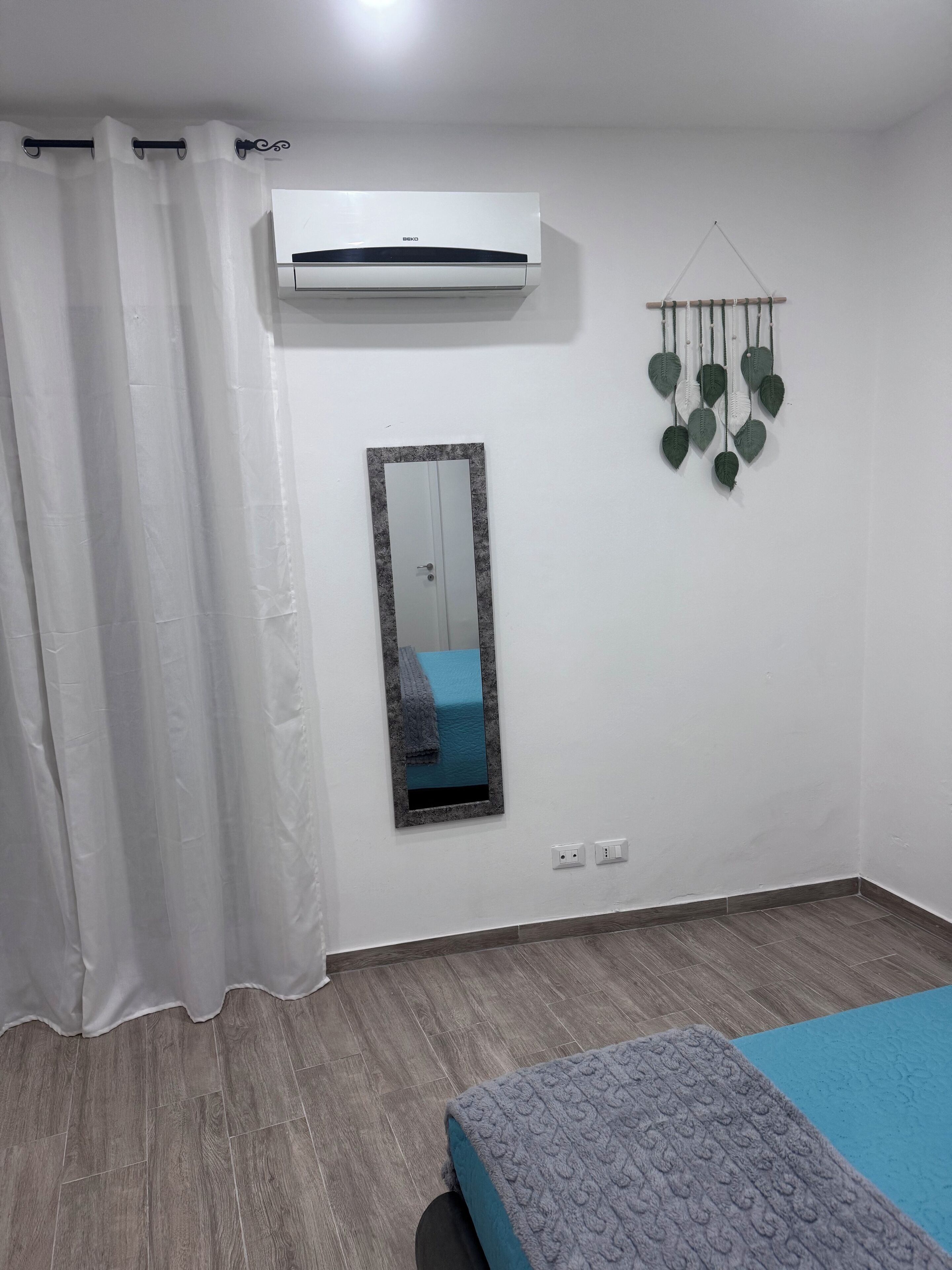 A bedroom with a bed, an air conditioner, a mirror, and a wall-mounted decoration.