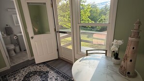 Un coin repas avec une table ronde et des chaises, un tapis à motifs et une vue sur un jardin, visible à travers une porte et une fenêtre.