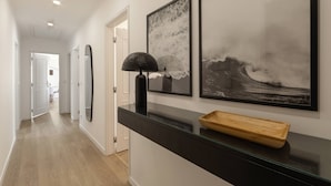 Un couloir moderne avec une console en verre, des œuvres d’art encadrées et un plateau en bois.