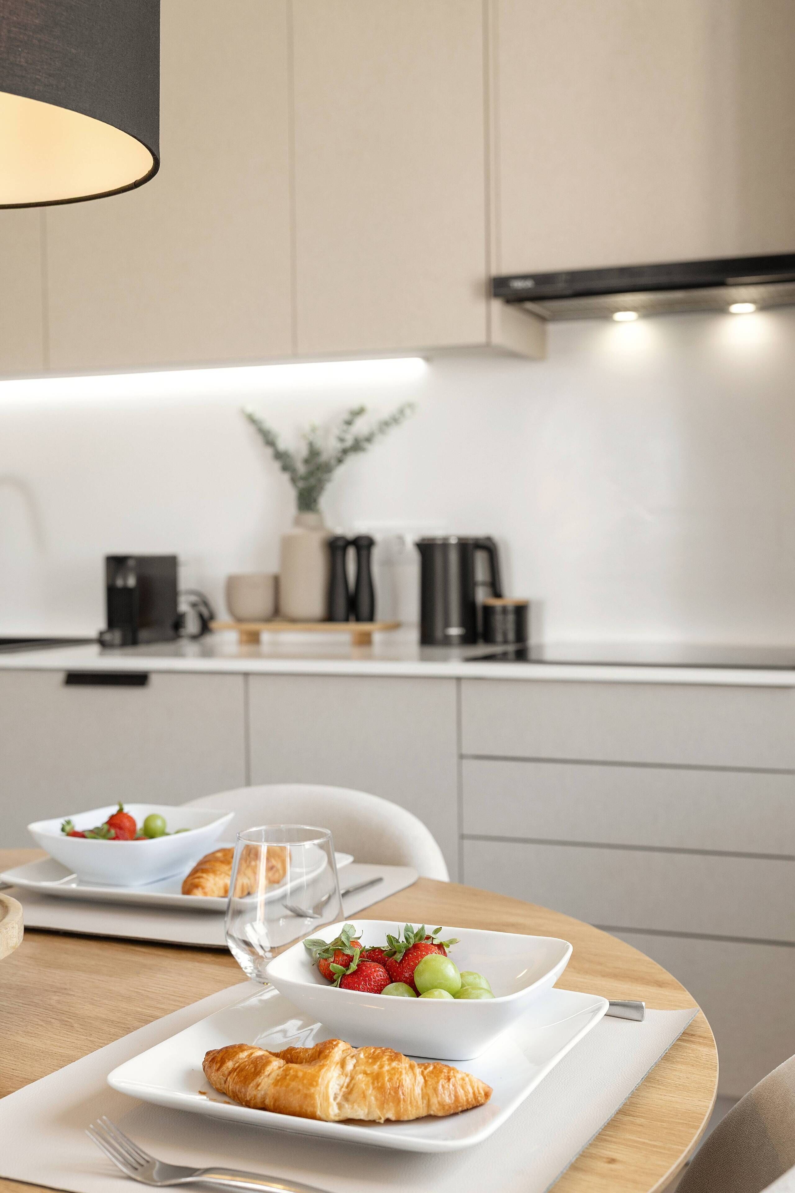 Eine moderne Küche mit Frühstücksecke, darunter Croissants, Obst und Kaffee.
