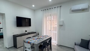 A modern living room with a dining area, a flat-screen TV mounted on the wall, and an air conditioning unit. - Apartment in the historic center of palermo (Palermo)
