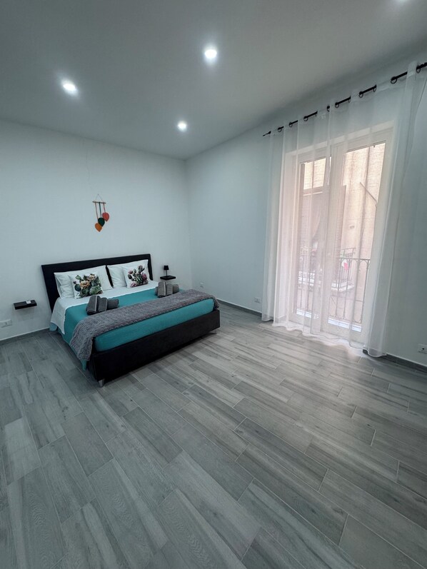 A bedroom with a bed, a bedside table, a hanging light fixture, and a window with curtains. - Cristofaro Home (Palermo)