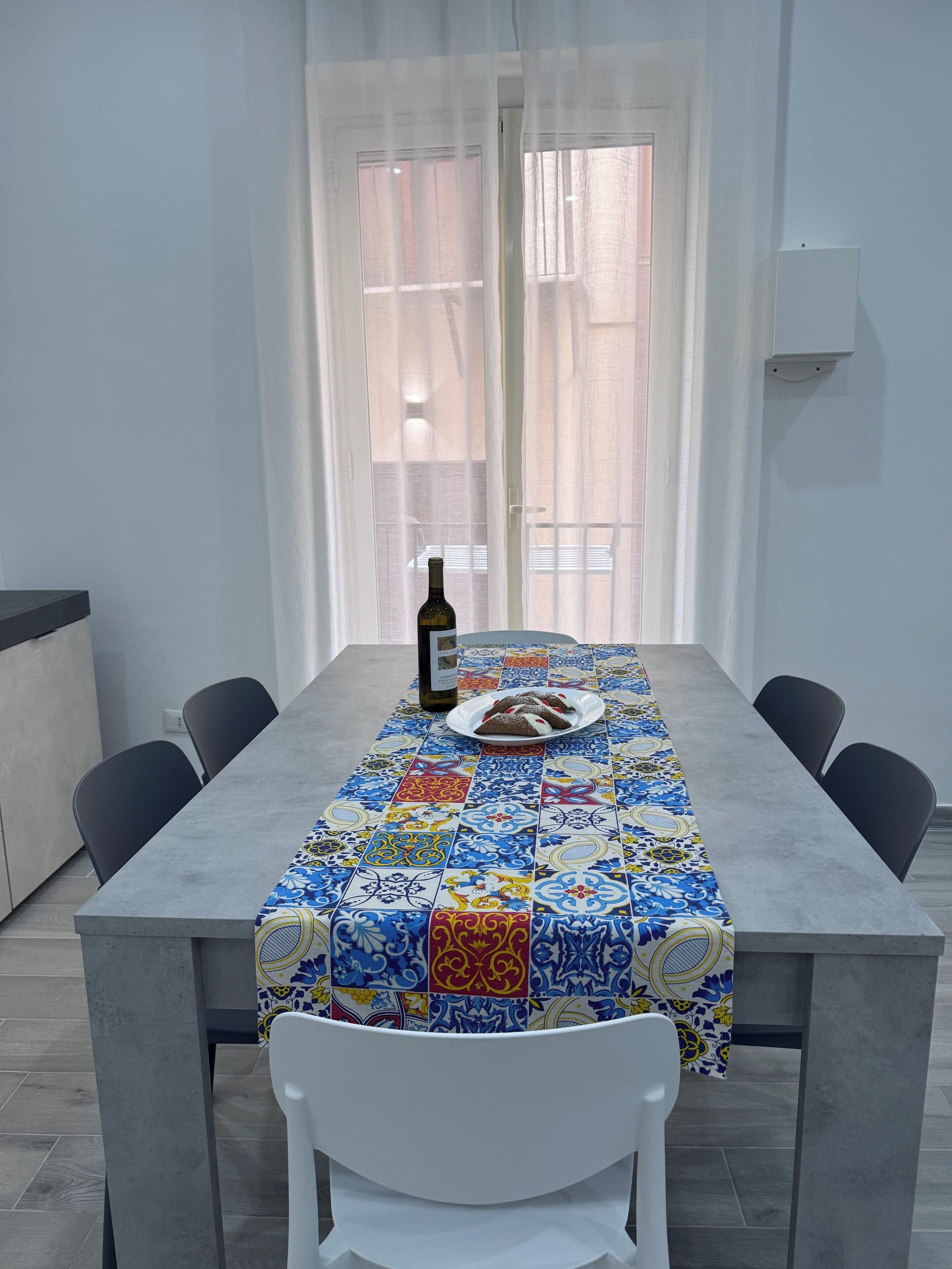 Une table à manger recouverte d’une nappe à motifs, une bouteille de vin et une assiette de nourriture.
