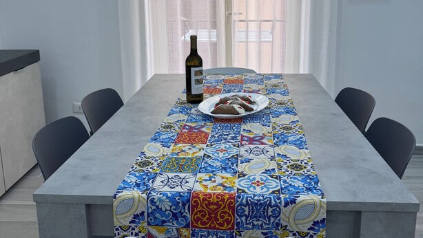 A dining table with a patterned tablecloth, a bottle of wine, and a plate of food.
