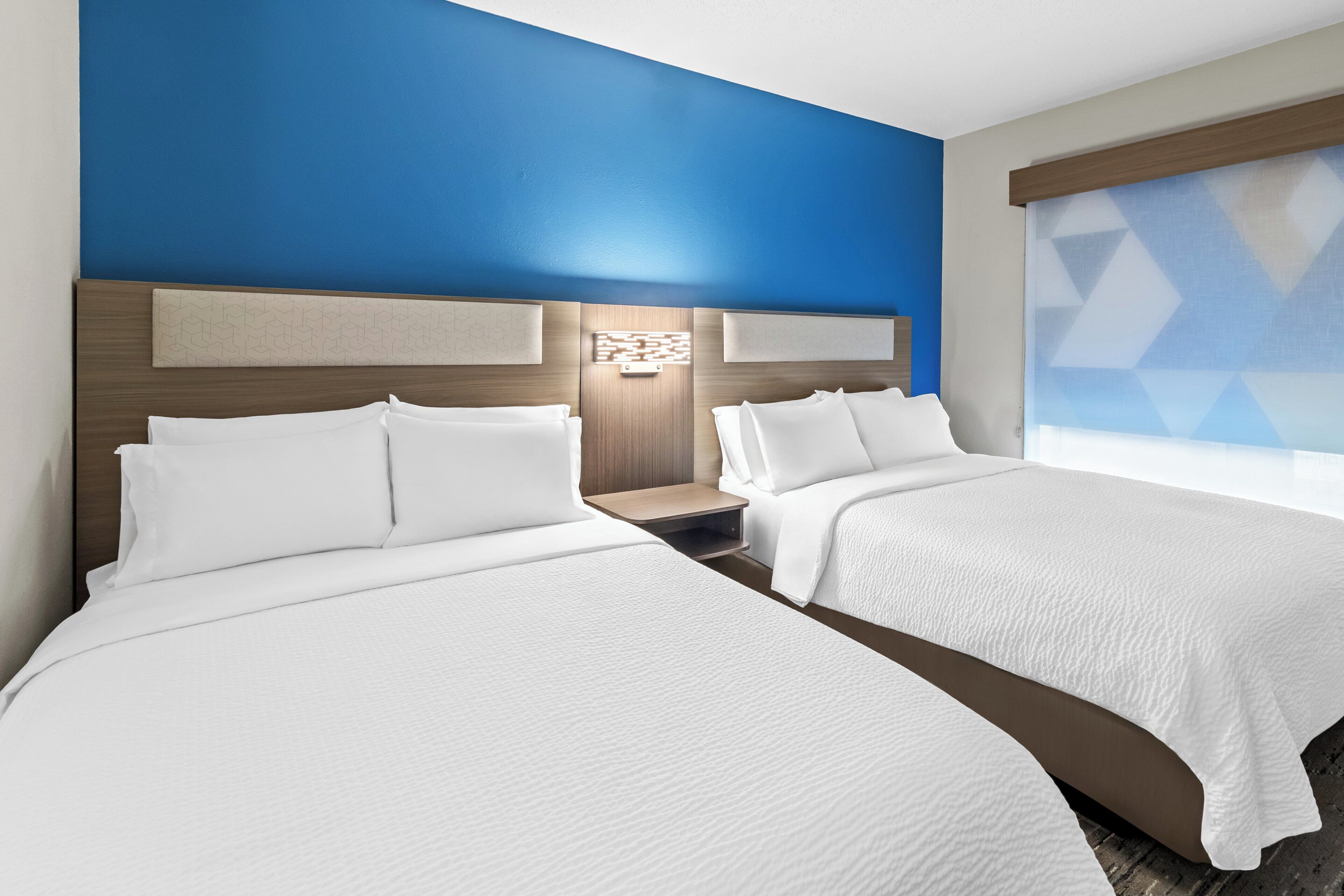 Habitación de hotel con dos camas, una pared de acento azul y una persiana con diseño geométrico.
