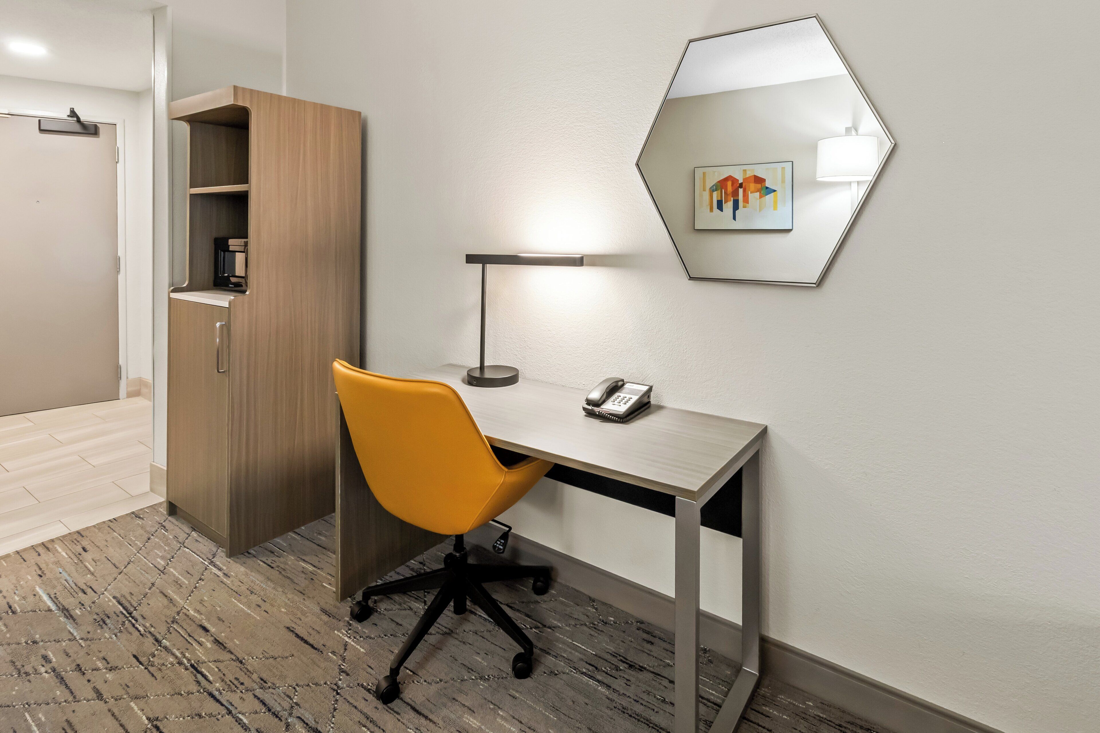 A hotel room with a desk, chair, and a cabinet.