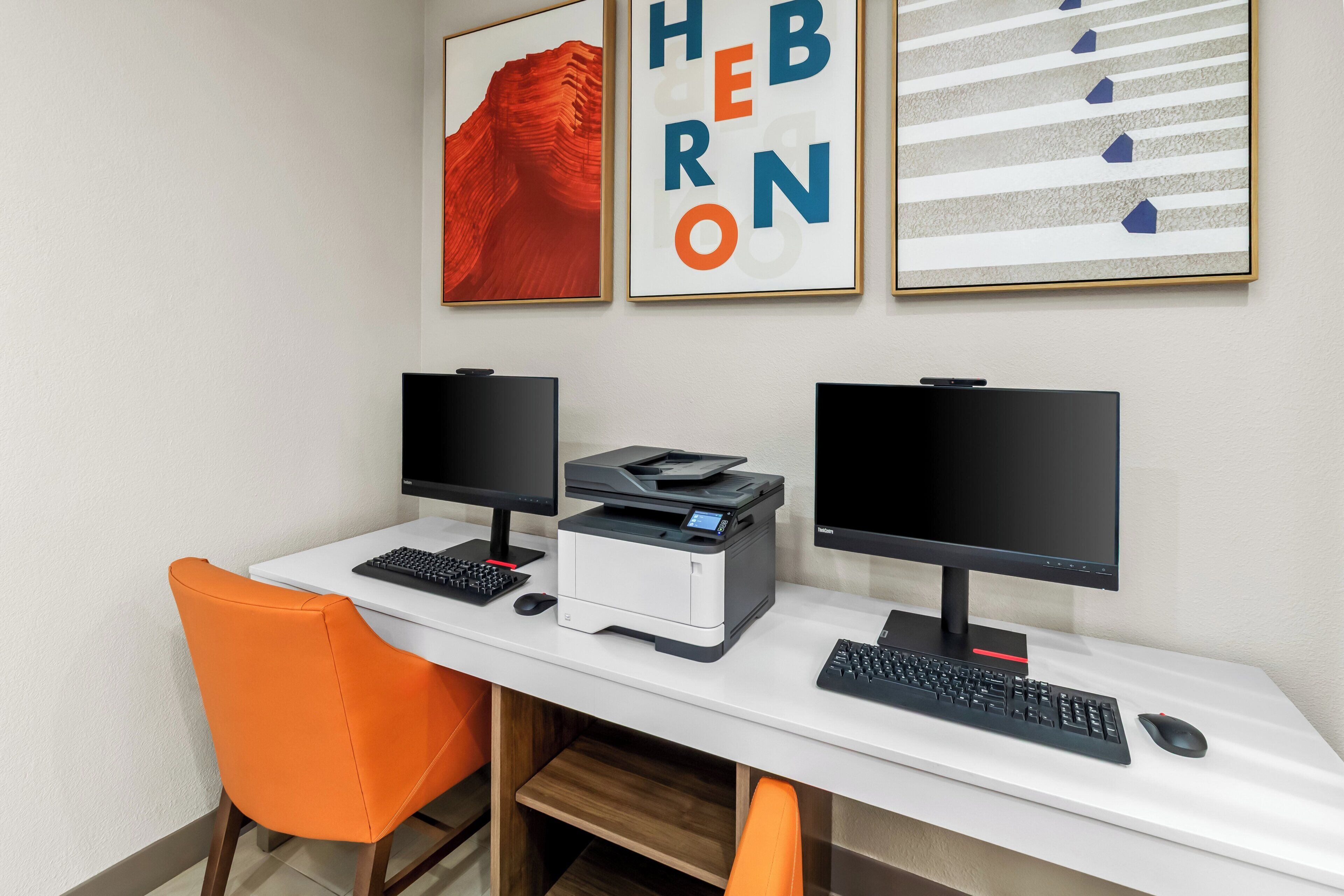 A workspace with two monitors, a printer, and an orange chair.