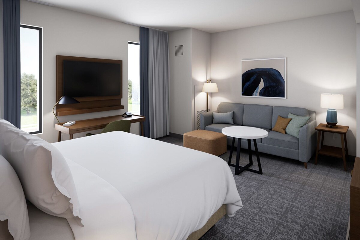 Une chambre d’hôtel avec un grand lit, un bureau doté d’un téléviseur à écran plat, un canapé, une petite table ronde et une lampe.