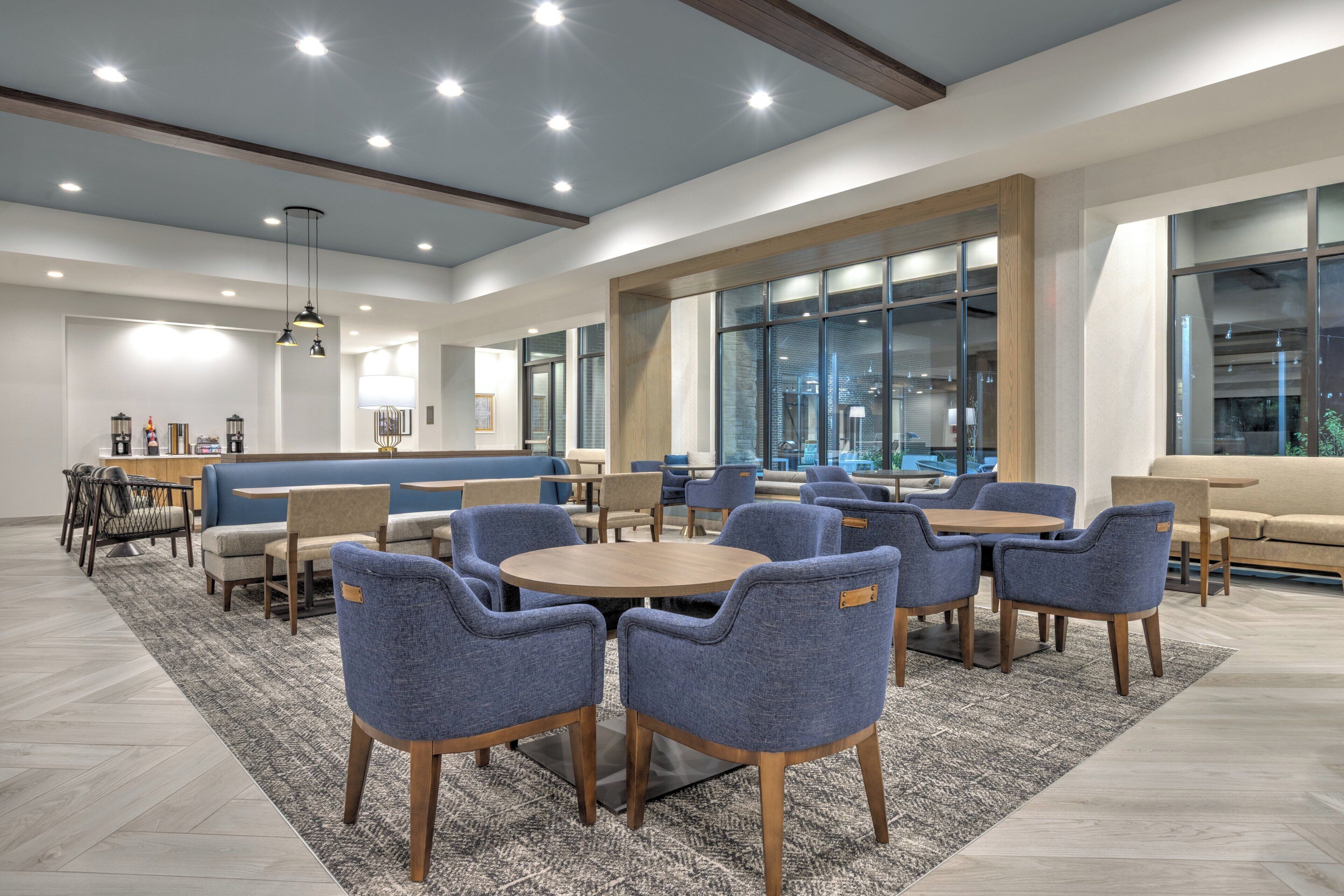 Un espace de détente intérieur moderne, avec des tables rondes et des chaises bleues, un bar et de grandes fenêtres offrant une vue panoramique.