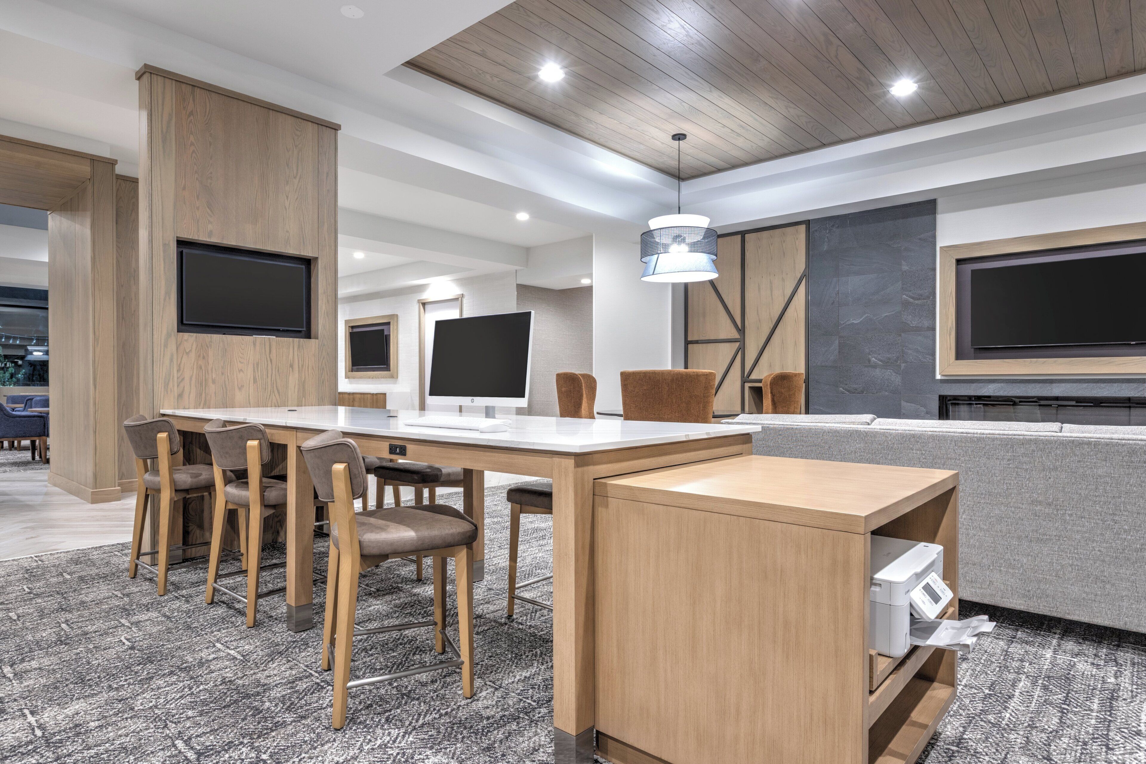 A modern office space with a long table, multiple chairs, a sofa, and two large flat-screen TVs mounted on the wall.