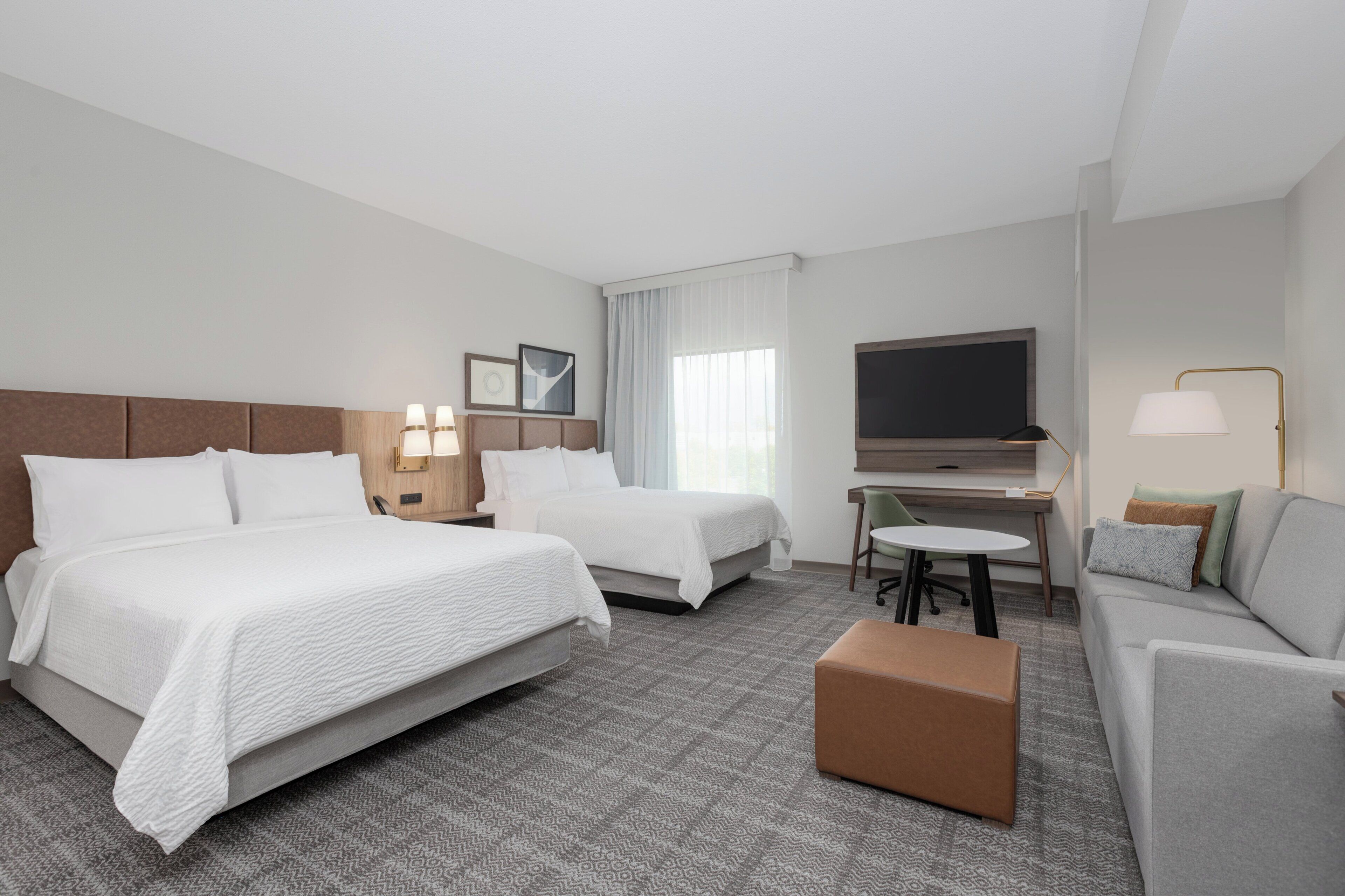 A hotel room with two beds, a desk, a TV, and a sofa.