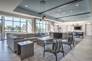 A spacious living area with a large sofa, coffee table, and chairs, a kitchen area with a dining table, and large windows offering a view of the outdoors. - Staybridge Suites Indianapolis South - Greenwood by IHG (Greenwood)
