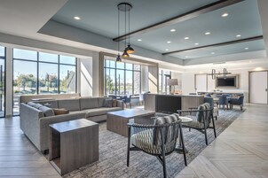 Un salón espacioso con un sofá grande, una mesa de centro y sillas, una cocina con mesa de comedor, y ventanas amplias que ofrecen vistas al exterior.
