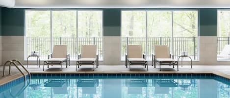 A swimming pool with four lounge chairs and large windows.