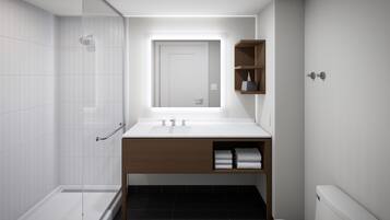 Un baño moderno con cabina de ducha de vidrio, un lavabo blanco con tocador de madera y un inodoro.