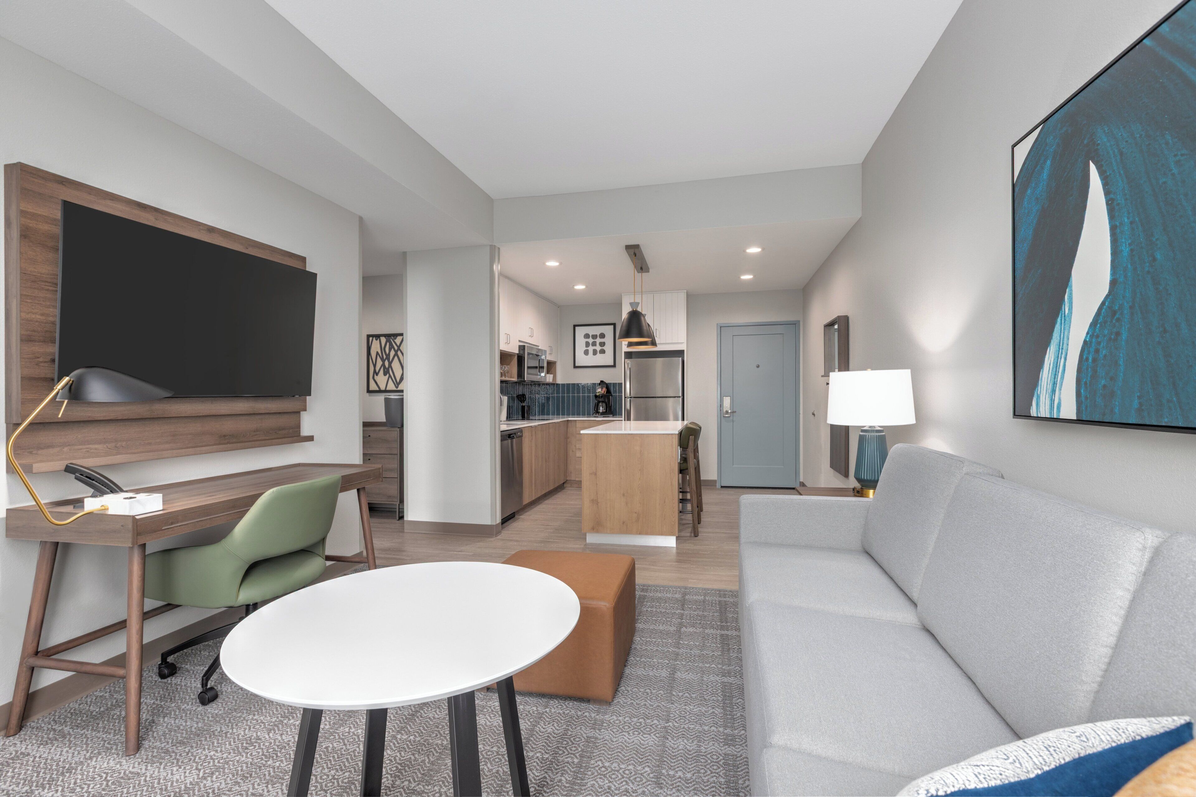 A modern living room with a grey sofa, a white coffee table, and a TV mounted on a wooden panel.