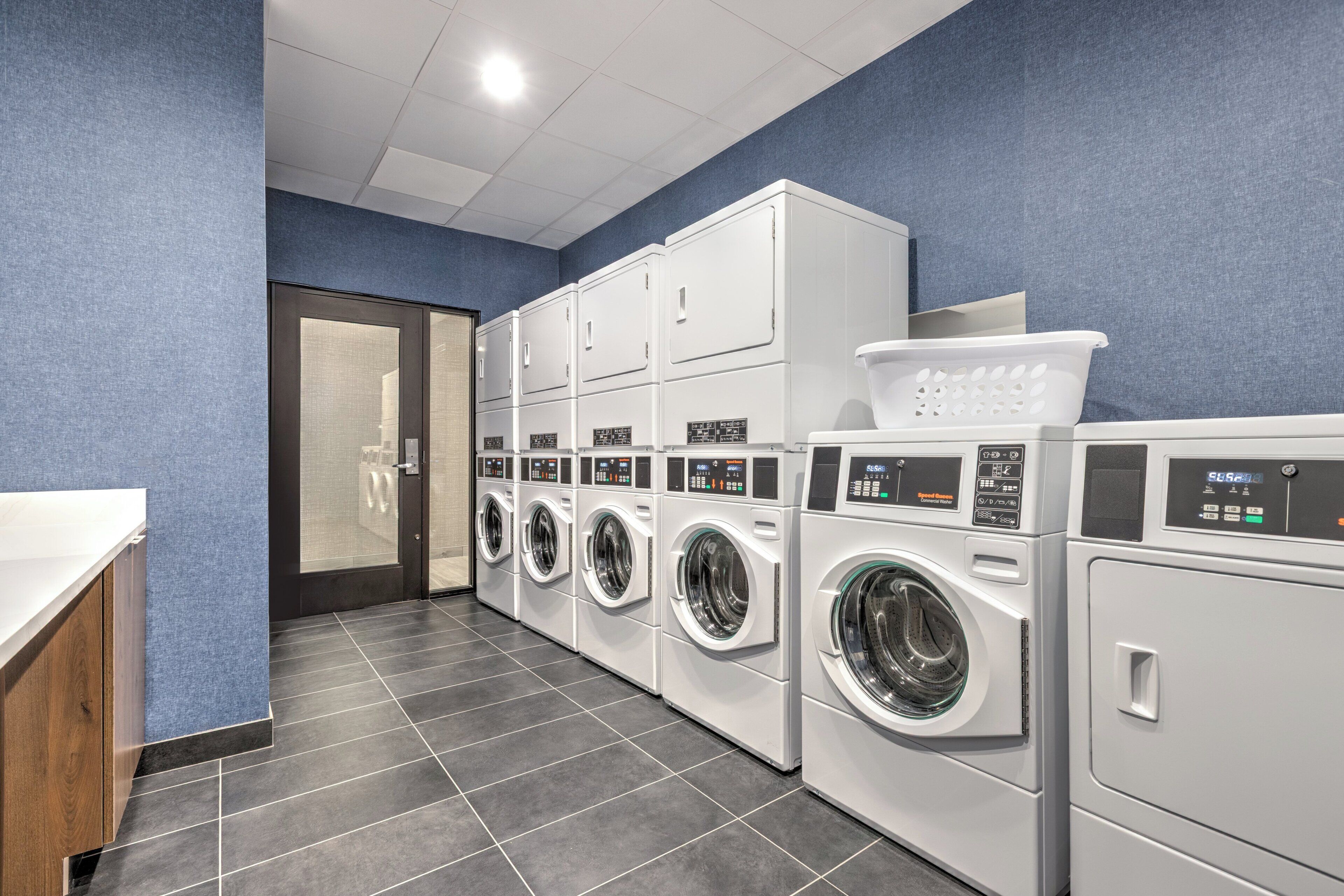 A laundry facility with multiple washing machines and dryers, a tiled floor, and a door leading to another room.