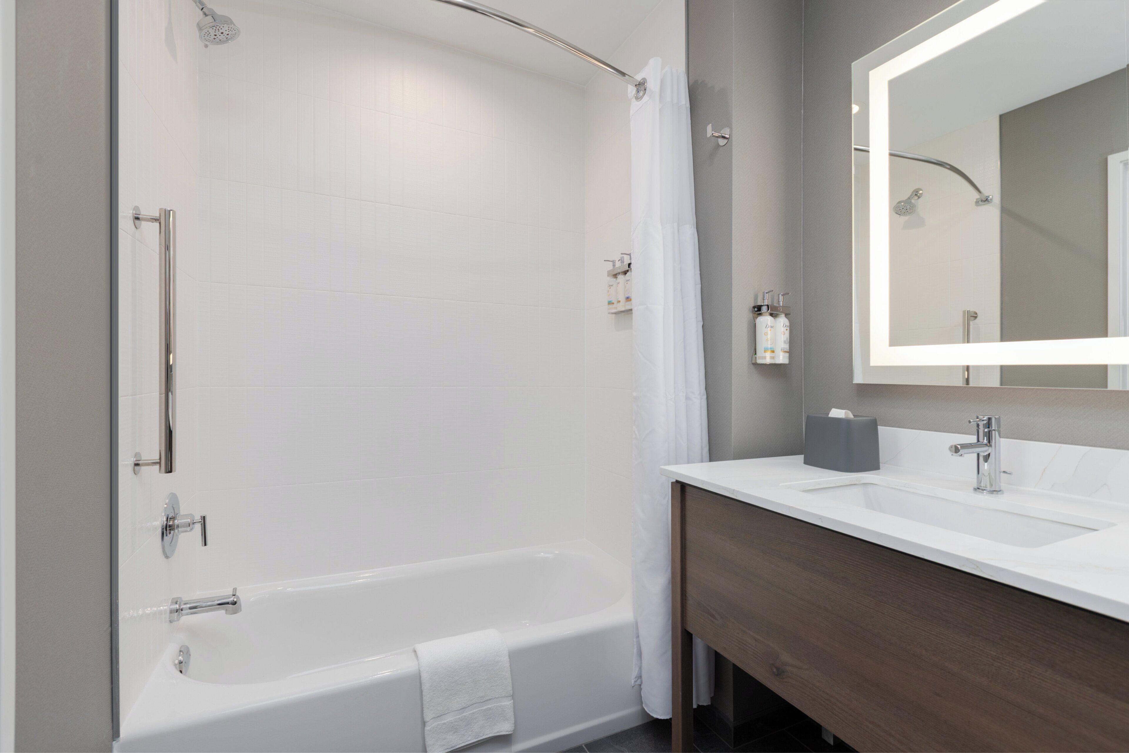 A modern bathroom with a bathtub, a vanity with a mirror, and toiletries.