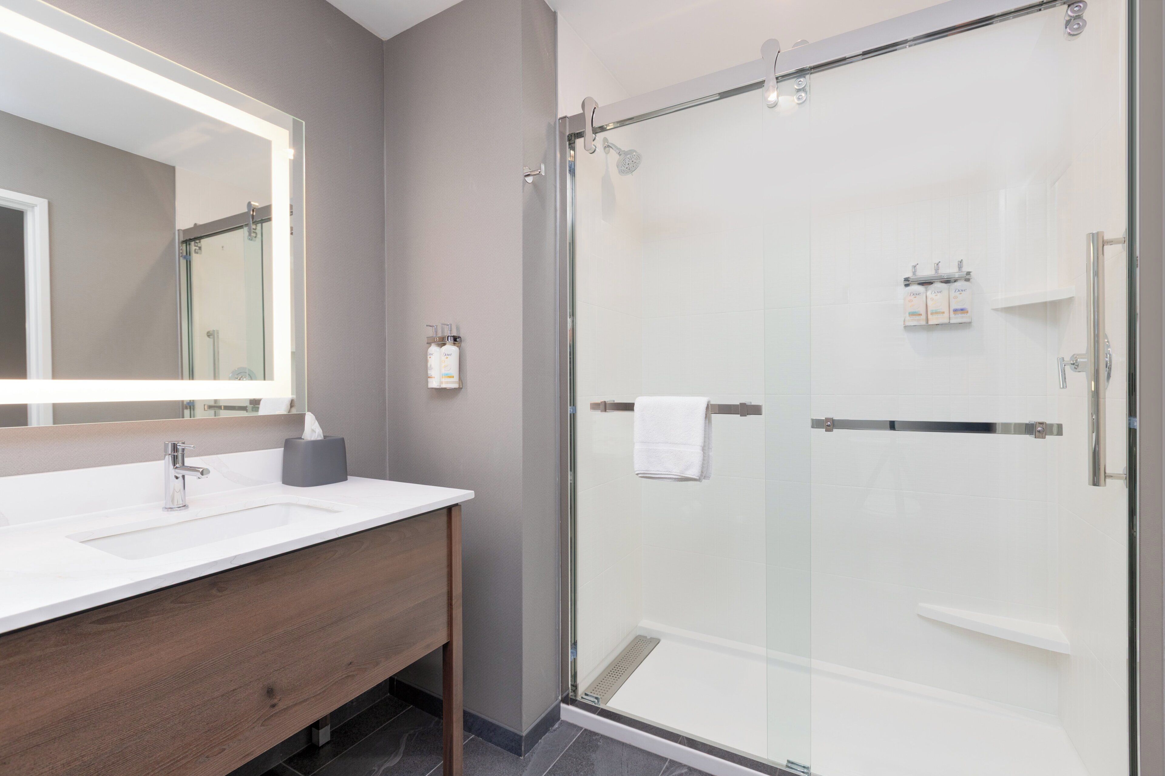 A modern bathroom with a glass-enclosed shower, a white sink with a mirror, and toiletries on the wall.
