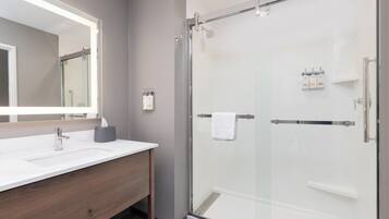 A modern bathroom with a glass-enclosed shower, a white sink with a mirror, and toiletries on the wall.