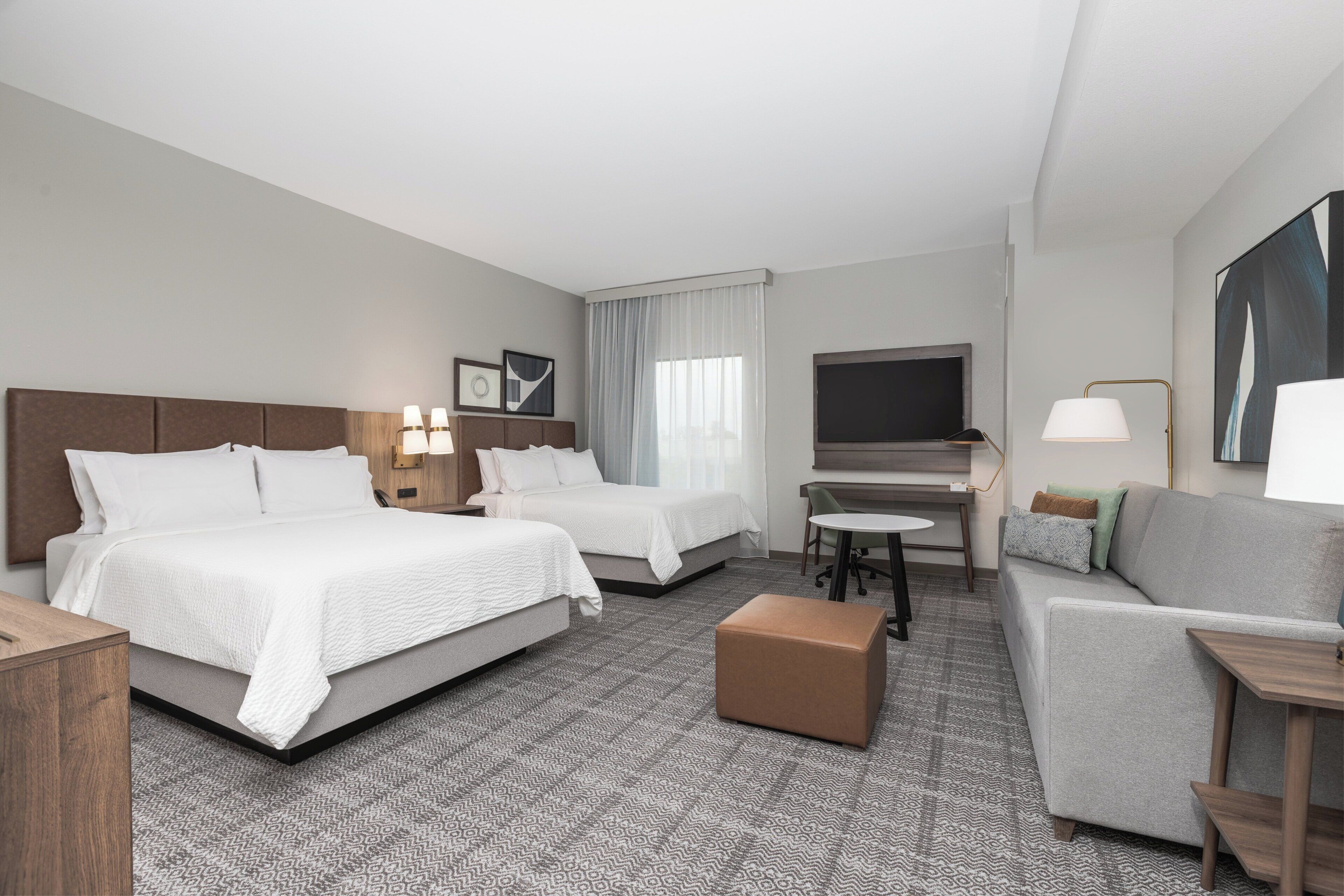 Ein Hotelzimmer mit zwei Betten, einem Schreibtisch, einem Fernseher und einem Sofa.