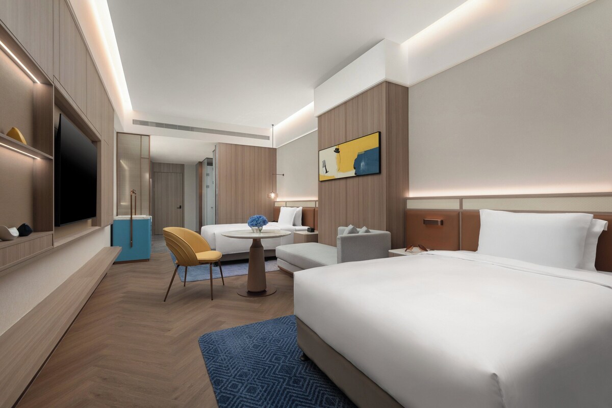 A modern hotel room with a large bed, a desk, a chair, a television, and a painting on the wall.