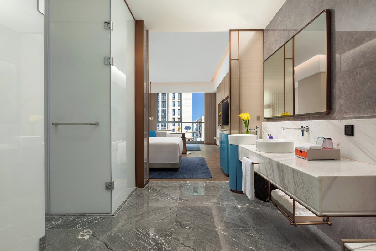 A modern bathroom with a large mirror, a marble countertop, and a view of a cityscape.
