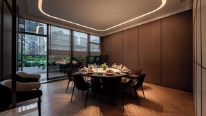 A modern dining area with a round table set for six, surrounded by black chairs. Large windows offer a view of a cityscape and greenery outside. - voco Chengdu Chunxi Road by IHG (Chengdu)