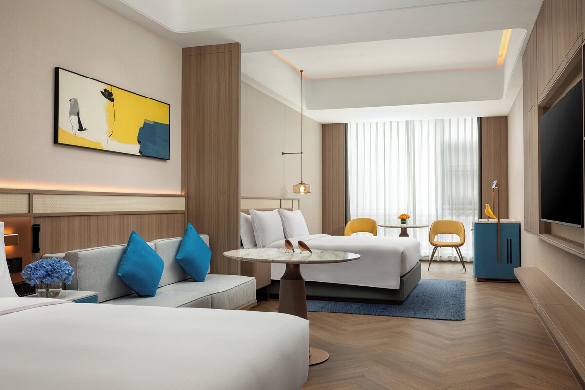 A modern hotel room with a large bed, a sofa, a small table, and a TV.