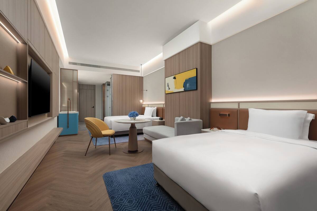 A modern hotel room with a large bed, a desk, a chair, a television, and a painting on the wall.