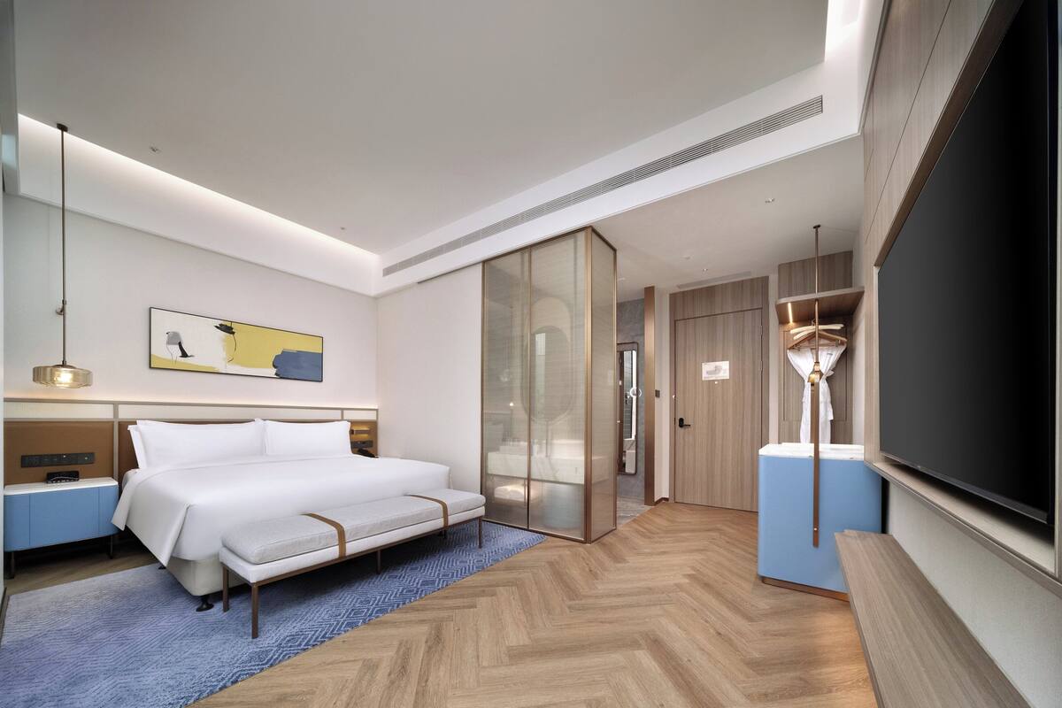 A modern hotel room with a bed, bedside tables, a TV, and a wardrobe.
