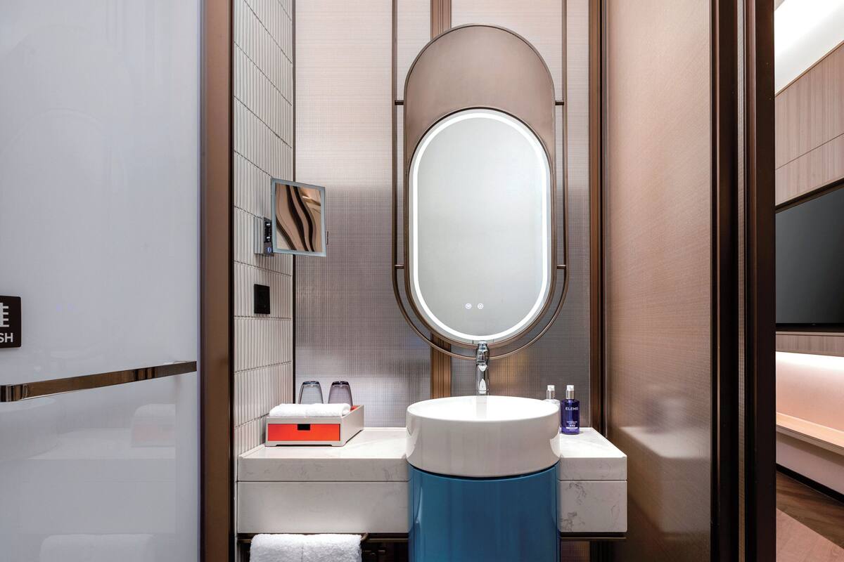 A modern bathroom with a large mirror, a sink, and a vanity. There is a towel rack and a bottle of hand soap on the counter.