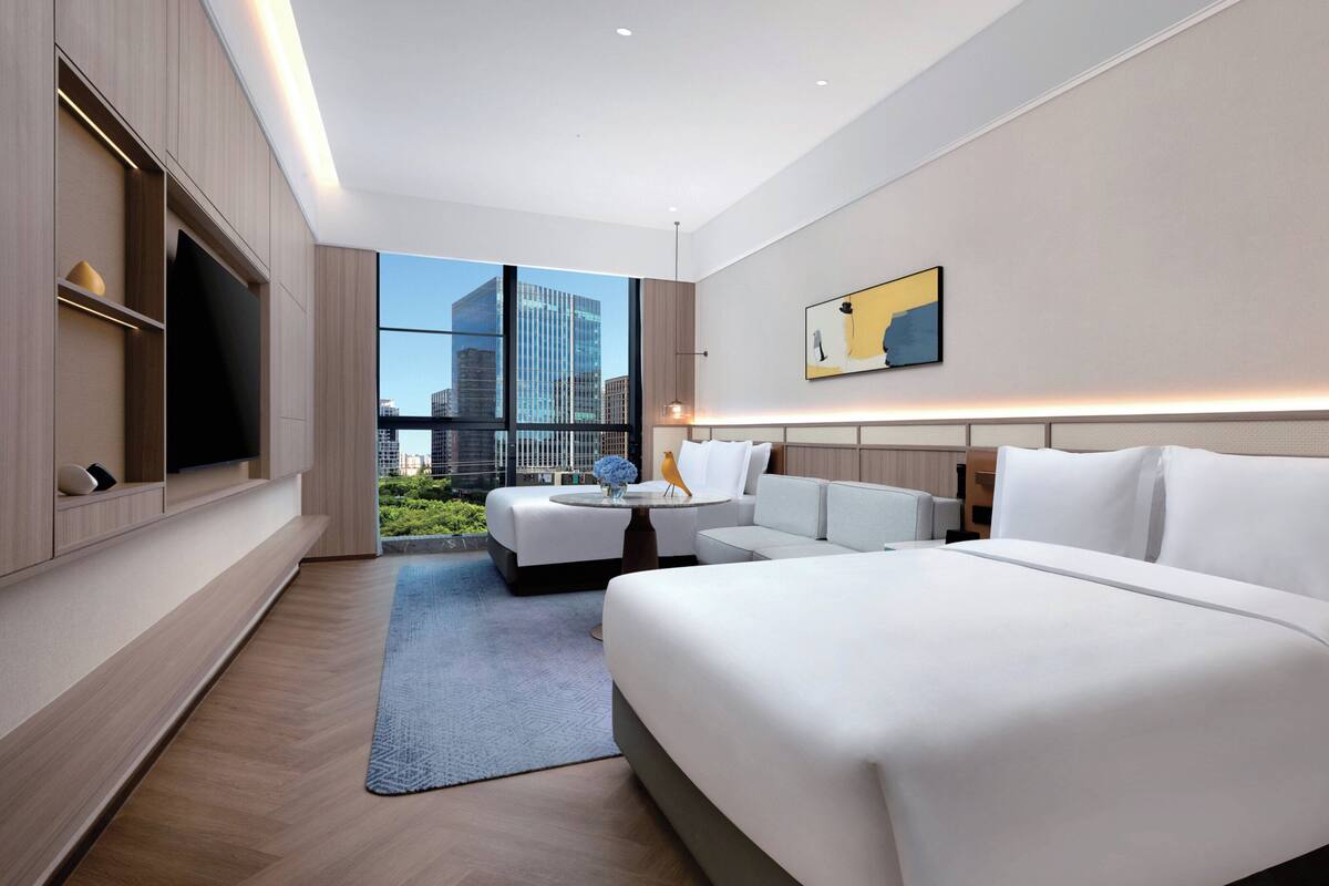 A modern hotel room with a large bed, a sofa, a TV, and a view of the cityscape.