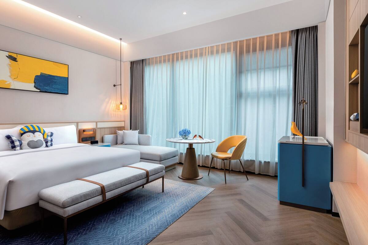 A modern hotel room with a large bed, a sofa, a small table with a vase, and a TV.