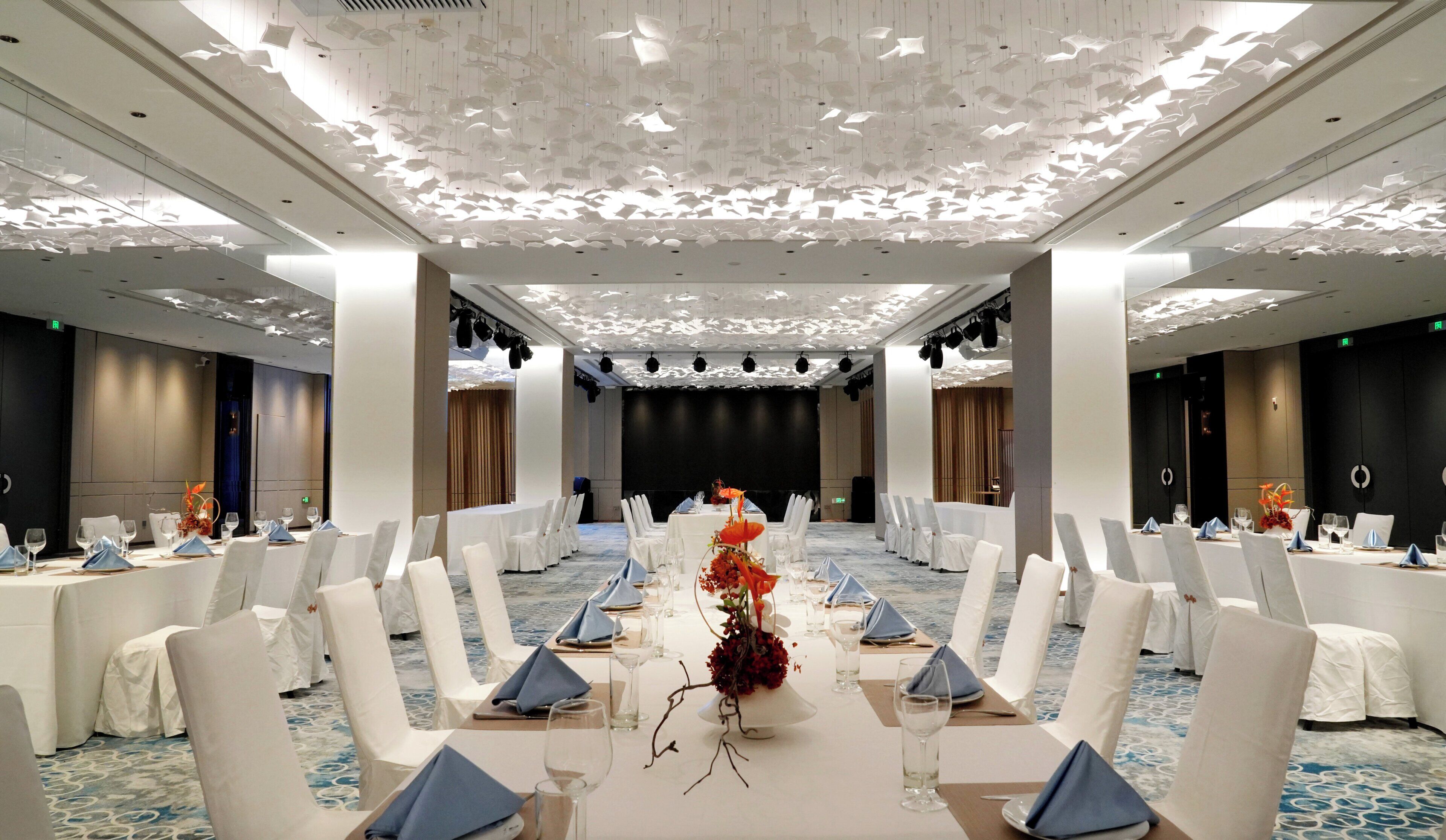 Un salón de conferencias con sillas y mesas blancas, y un escenario.
