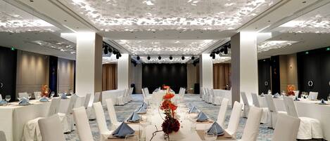 Un salón de conferencias con sillas y mesas blancas, y un escenario.