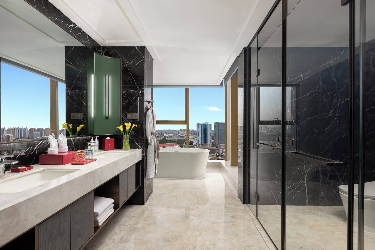 Ein modernes Badezimmer mit einer großen Badewanne, einem Waschtisch mit Spiegel und Blick auf die Stadt durch große Fenster.