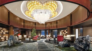 A spacious lobby with a central staircase, seating areas, and a large chandelier.