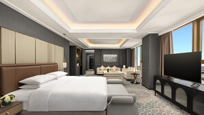A modern hotel room with a large bed, a sofa, a TV, and a city view.