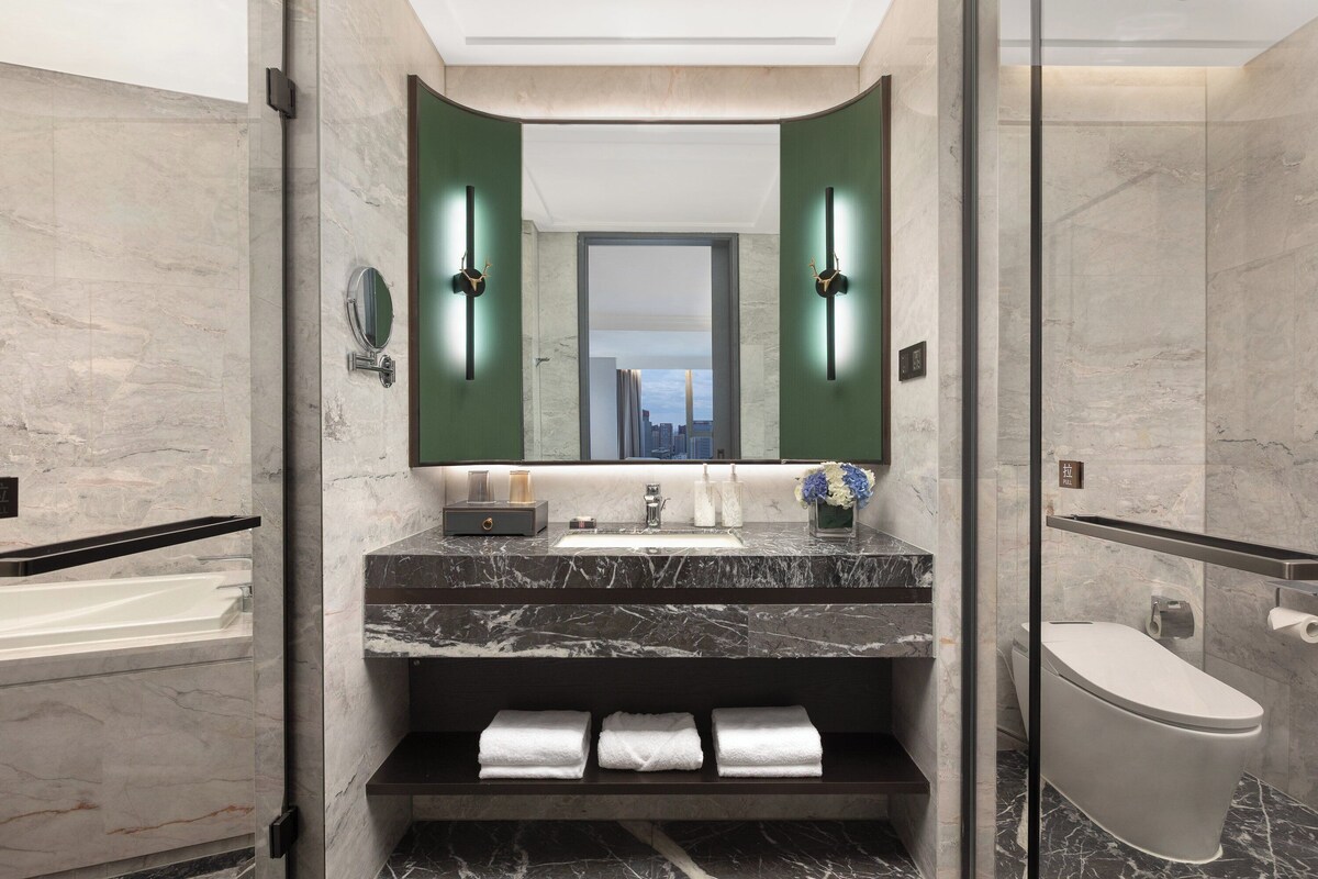 A modern bathroom with a marble sink, a large mirror, and a glass-enclosed shower.