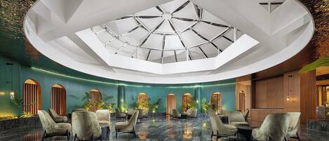 A spacious lobby with a high ceiling, a central skylight, and a seating area with modern chairs.