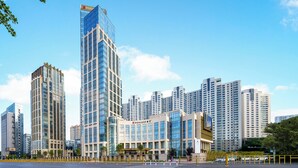 A modern high-rise building with a glass facade, surrounded by other tall buildings, and a clear sky.